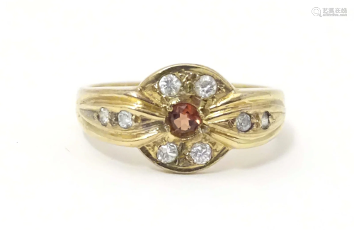 A yellow metal ring set with central garnet bordered by whit...