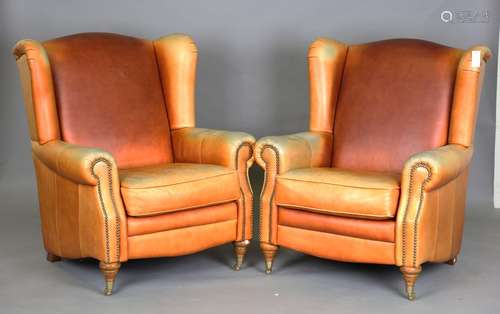 A pair of modern tan leather armchairs with brass studded bo...