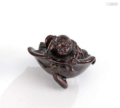 A FINE WOOD NETSUKE OF AN ONI SITTING INSIDE A LOTUS LEAF