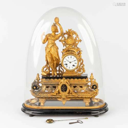 A mantle clock made of gilt spelter, standing under a glass ...
