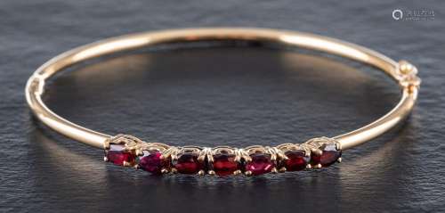 A 9ct gold bangle set with oval-shaped, mixed-cut garnets:, ...