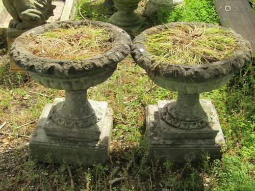 A pair of weathered composition stone garden urns, the squat...