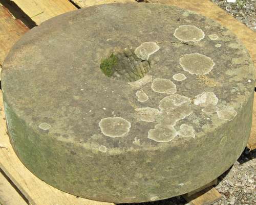 A weathered natural stone millstone with circular central cu...