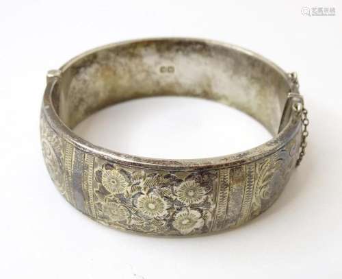 A silver bracelet of bangle form with engraved floral and fo...