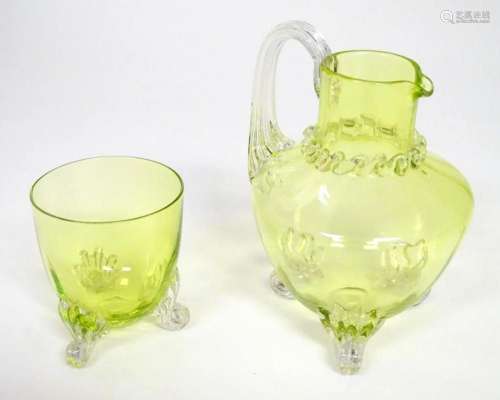 A yellow glass water jug with clear glass handle and feet, t...