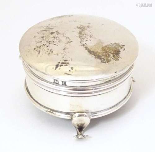 A small silver ring box of circular form with hinge lid stan...