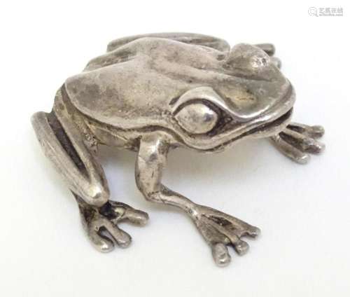 A white metal model of a frog. Approx. 1 1/2" long