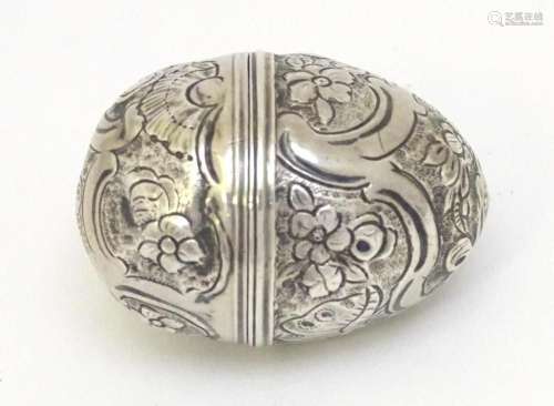A white metal nutmeg grater of egg form with embossed floral...