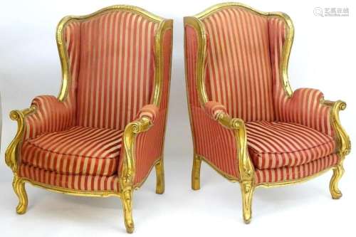 A pair of mid 20thC large gilt wingback armchairs, having mo...