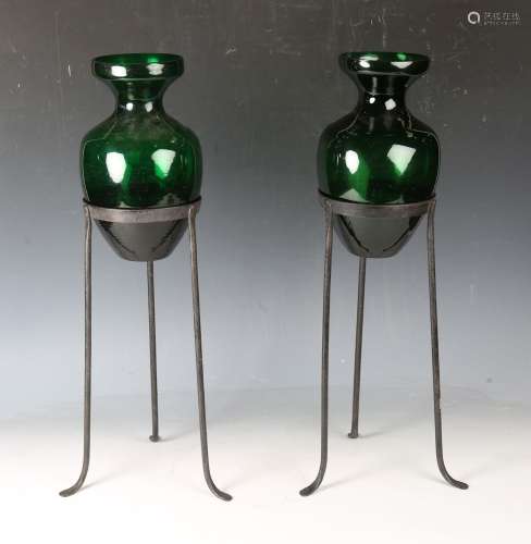 A pair of green glass ornamental urns, each raised on a wrou...