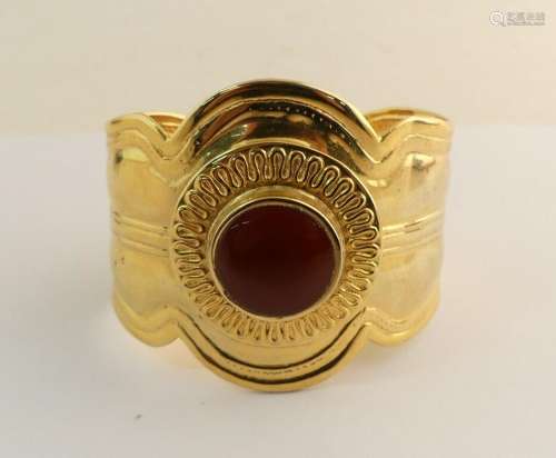 Bracelet manchette en métal doré orné d'une pierre brune.