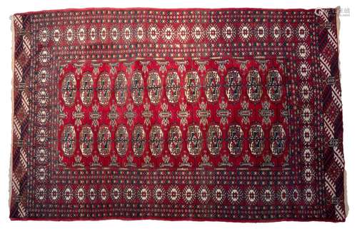 A MIDDLE EASTERN PERSIAN BOKHARA WOOL RUG. Red ground with c...