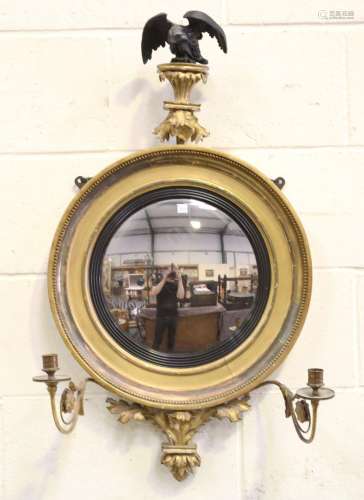 A Regency giltwood convex wall mirror with an ebonized eagle...