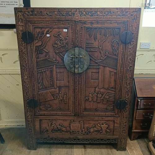 A Chinese two door wardrobe, carved a town scene with figure...