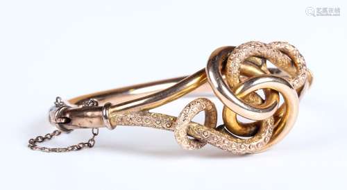 A gold oval hinged bangle, the front in an interwoven knot d...