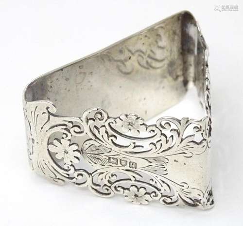 A silver napkin ring of triangular form with floral and foli...