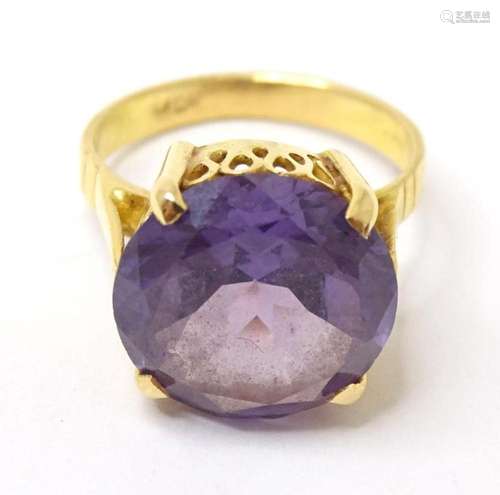 A yellow metal ring set with central purple stone. Indistinc...