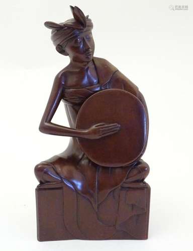 An Indonesian wooden carving modelled as a seated man playin...