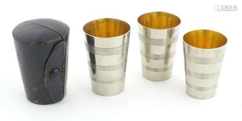 Three 20thC silver plate tot cups / beakers in fitted leathe...