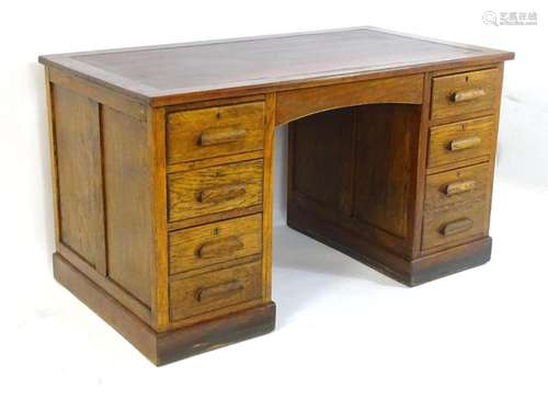 An early 20thC oak pedestal desk with an inset leather top a...