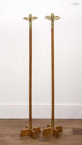 A pair of oak and brass tall floor standing candle stands in...