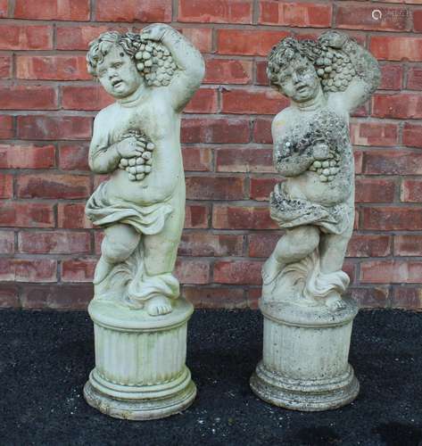 A pair of reconstituted stone cherubs, each modelled arm rai...