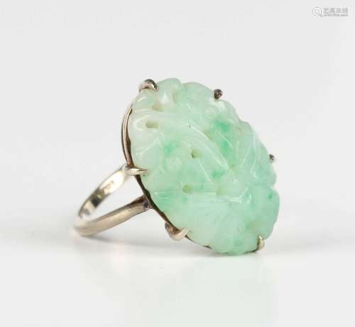 A white gold ring, claw set with an oval jade with carved an...