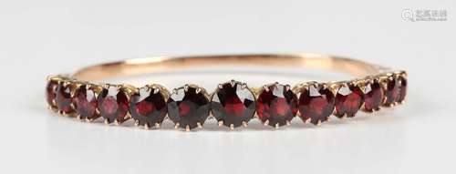 A gold and garnet oval hinged bangle, the front claw set wit...