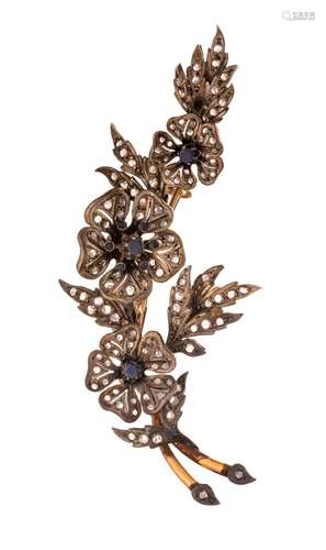 A silver and gold floral-shaped brooch, set with blue sapphi...