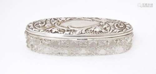 An oval cut glass dressing table jar with embossed silver li...