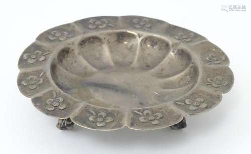 A Mexican silver dish with floral detail and raised on three...