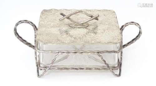 A glass and silver plate butter dish with textured detail an...