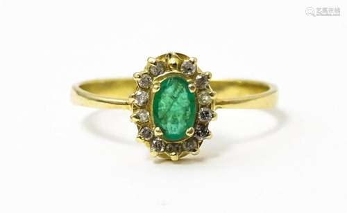 A gold ring set with central emerald bordered by diamonds. R...