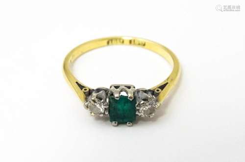 An 18ct gold ring set with central emerald flanked by diamon...