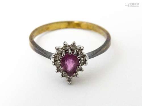 A yellow metal ring set with pink sapphire flanked by diamon...