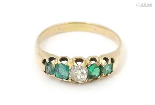An 18ct gold ring set with central diamond flanked by two em...