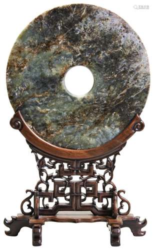 A MOTTLED JADE BI DISC ON HUANGHUALI STAND 18TH/19TH CENTURY...