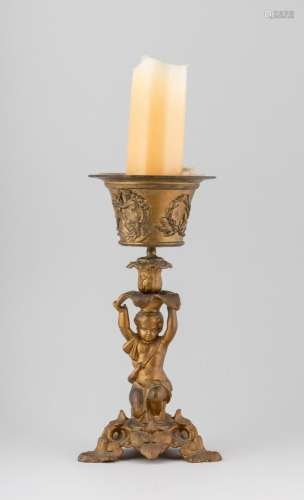 A gilt metal candle stand in the form of a cherub supporting...