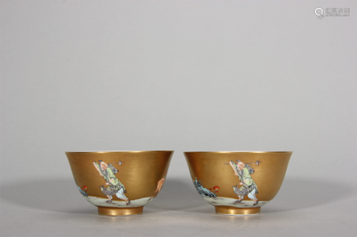 A pair of gold ground famille rose figure porcelain tea cups...