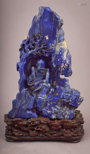 Lapis Lazuli carving. China. Late 19th century. Figure of a Luohan in a mountain grotto. Extensive inscription at the back. Finely carved hardwood stand. 9