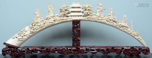 An exceptional Chinese richly carved ivory tusk, depicting various temples and pagodes in a montanious landscape, on a matching carved wooden base, first half 19thC, H 48,5 (without base) - 56,5 (with base) - W 152 cm