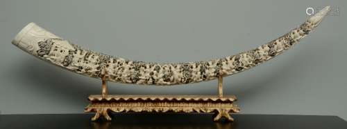 An impressive Chinese ivory tusk, richly carved with an animated scene, on a matching wooden base, scrimshaw decorated, first half 20thC, H 57,5 (with base) - L 159,5 cm