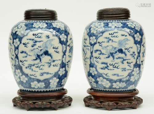 A pair of Chinese blue and white vases and wooden covers, decorated with prunus blossoms, the roundels painted with Fu lions, on a wooden base, 19thC, H 37 cm (with base) / H 29,5 cm (without base) (one vase with chips and cracks)