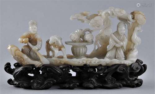 Jade carving. China. 19th century. Grey stone with tan markings. Carving of a raft with two female Immortals and various symbols of longevity. Carved fitted hardwood stand. 8