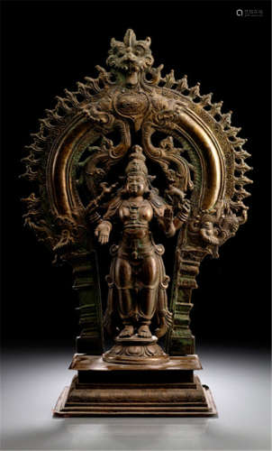A BRONZE FIGURE OF SHIVA, South-India, 19th/20th Ct., standing in samabhanga on a lotus base placed on a separate cast base, his four arms radiating around his body, both secondary ones holding axe and deer, wearing dhoti, bejewelled, his face displaying a serene expression and an elaborate back-slab behind - Property from an old Bavarian private collection, acquired between 1960 and 1990