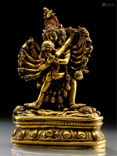 A GILT-BRONZE FIGURE OF CAKRASAMVARA, TIBET, standing in alidhasana on a pair of divinities reclining on a lotus base, embracing his consort, his principle hands holding vajra and ghanta, the others various attributes and his four-faced head displaying severe expressions, resealed-Former property from a European private collection-Minor wear, very slightly chipped, small repairs