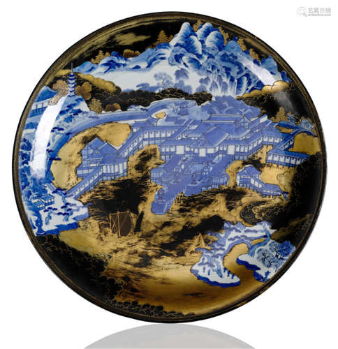 AN ARITA BLACK AND GOLD LACQUERED PORCELAIN CHARGER, Japan, 19th ct. Well painted in underglaze blue with a detailed view of Itsukushima Shrine enriched with gold lacquer foliage, clouds and waves, in a border of vermiculi, the underside with three tendrils. The island shrine north west of Hiroshima Bay was established in the sixth century. Expanded and rebuilt in the mid 16th century, it is a UNESCO World Heritage Site. The highest peak on the island of 12 square miles, Mt. Misen (527m) forms a backdrop to the temple complex. - Property from a French private collection, acquired at Mellors and Kirk, 15th Sep 2011, lot 172 - Minor wear to lacquer
