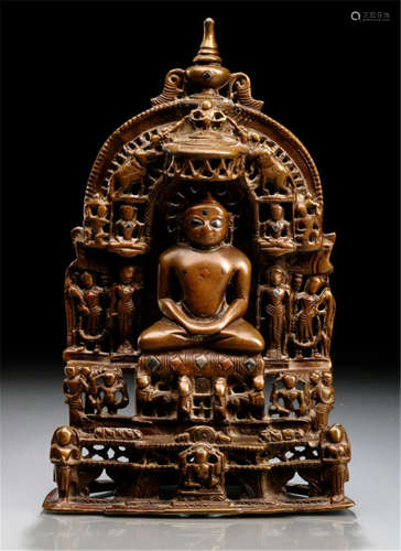 A BRONZE SHRINE DEPICTING A JAIN TIRTHANKARA, NORTHWEST-INDIA, 16th/17th Ct., the central Jain Tirthankara is seated in vajrasana on a cushion set with silver plaques, placed on a throne, both hands in dhyanamudra, his face inlaid with silver eyes and urna, parasol with trumpeting elephants above and surrounded by various figures, the reverse with inscriptions - Property from a German private collection - Minor wear, slightly chipped