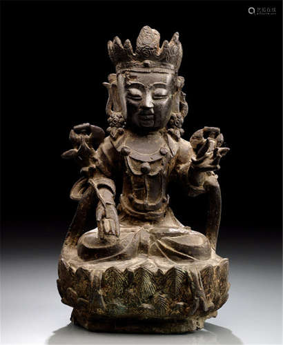 A BRONZE FIGURE OF GUANYIN, CHINA, late Ming dynasty, seated in vajrasana on a lotus base, both hands holding stems of lotuses flowering along the upper arms supporting manuscripts, wearing dhoti, cape, bejewelled, his face displaying a serene expression and his hair secured with a tiara-Property from an old German private collection, assembled between 1950 and 2000-Wear, minor damage due to age