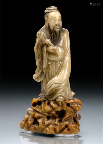 A CARVED SOAPSTONE MODEL OF A STANDING IMMORTAL ON A ROCK